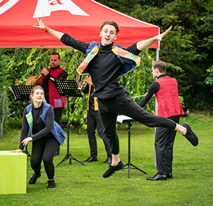 A performer leaps into the air in a garden setting
